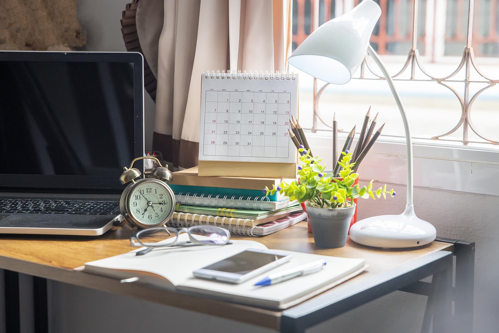  Desk with books, a laptop and a clock on it representing giving yourself time and patience while working through anxious feelings. Learn tools to make your work environment anxiety free with anxiety therapy online in Utah. 84108 - 84317 
