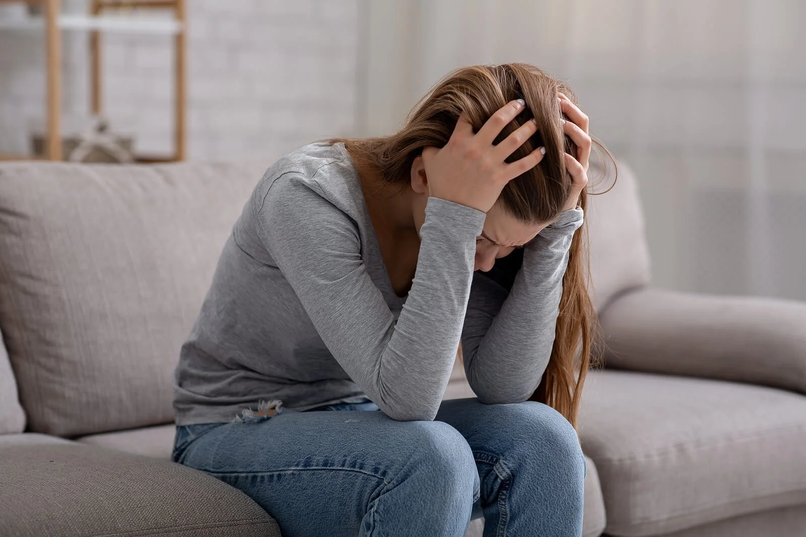  Woman sits on sofa with head in her hands looking stressed. Suffering from pain could lead a person to trauma therapy in Austin, TX with a skilled trauma therapist. You can get help with online therapy in Texas here.  